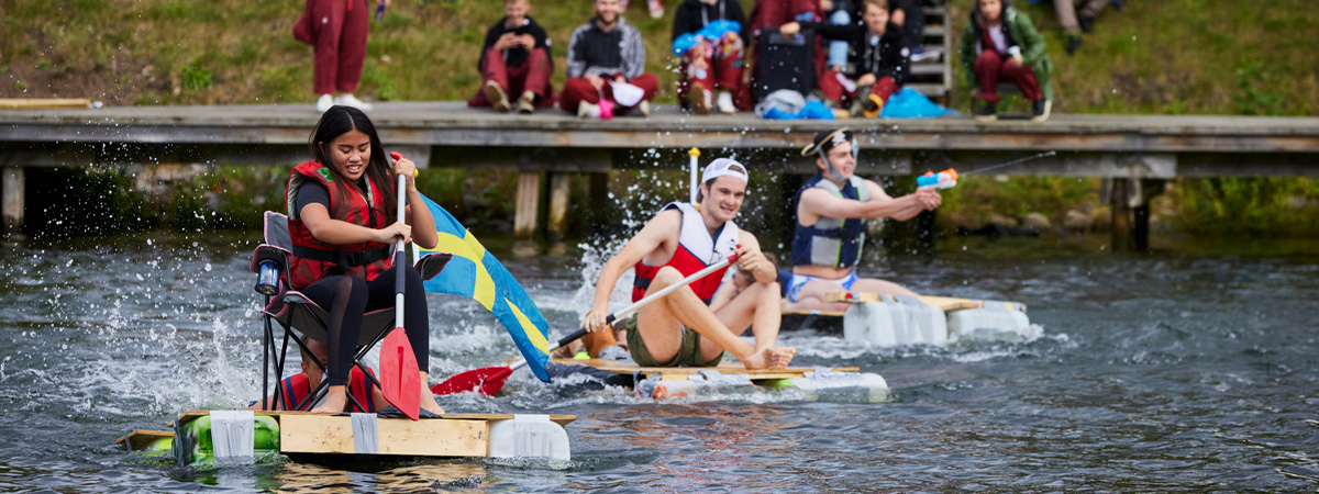 Tre studenter sitter på små flottor i en älv och ror